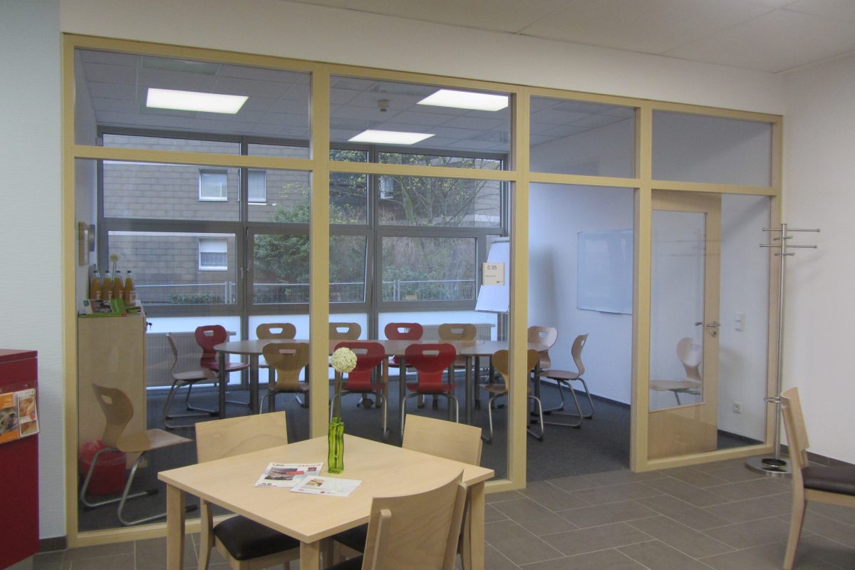 Blick in einen hellen Seminarraum mit roten Stühlen und Glastrennwand.