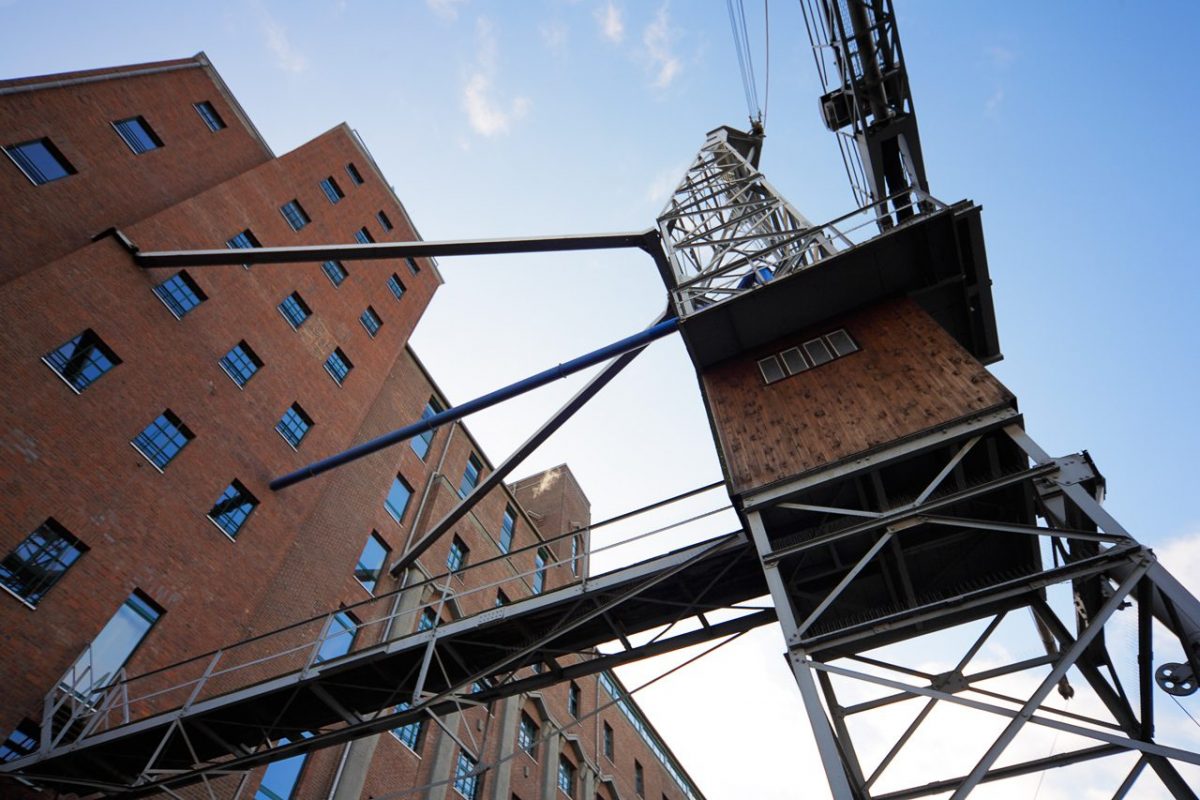 Backsteingebäude mit historischem Kran und Stahlkonstruktion im Vordergrund.