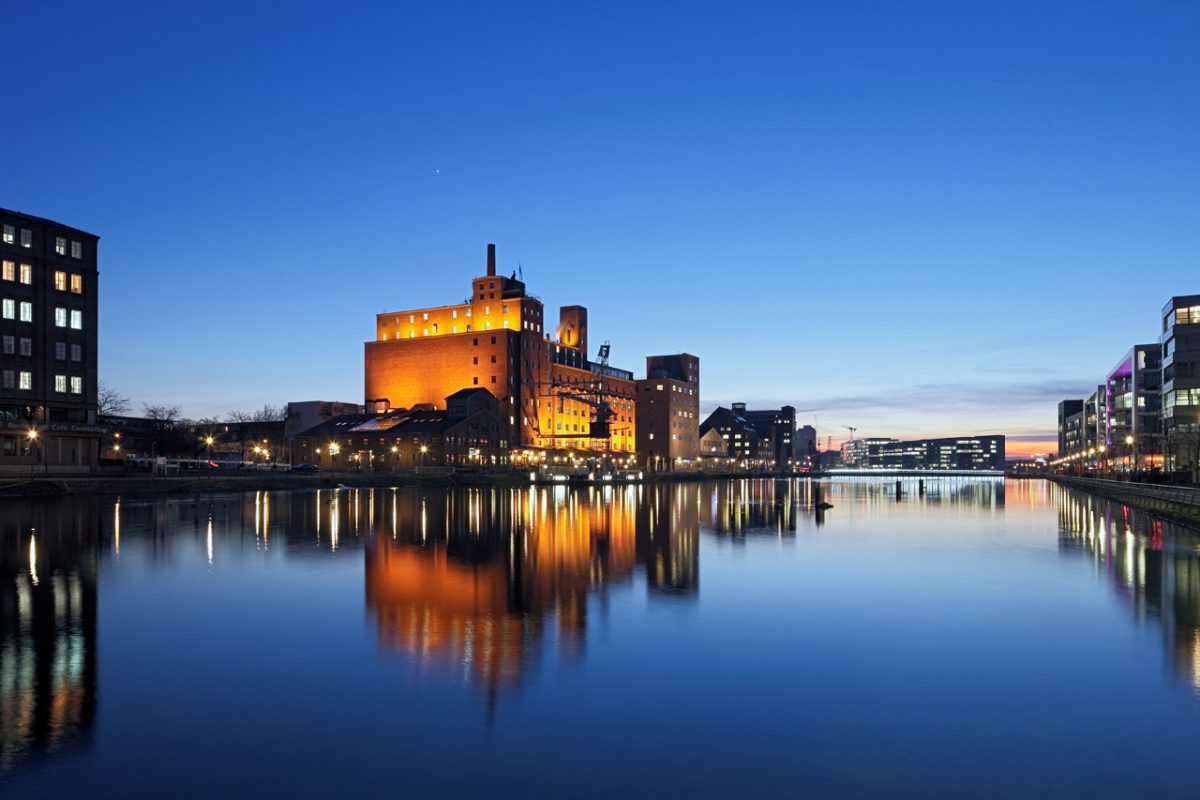Backsteingebäude am Hafenbecken mit Schornstein und Krananlage bei einbrechender Dunkelheit