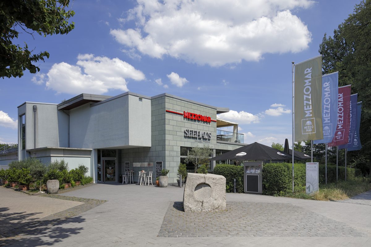 Modernes Gebäude mit Restaurant „Seehaus“ und Stein-Skulptur davor.