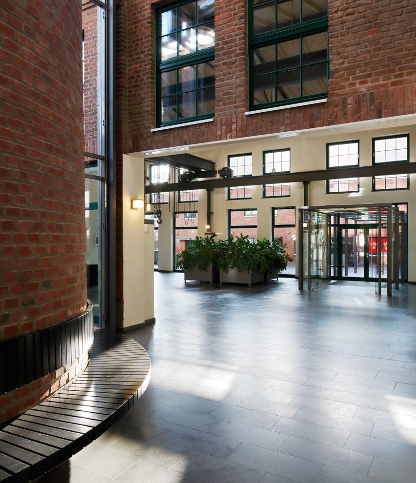 Heller Eingangsbereich mit roten Backsteinwänden und Rundbank aus Holz.