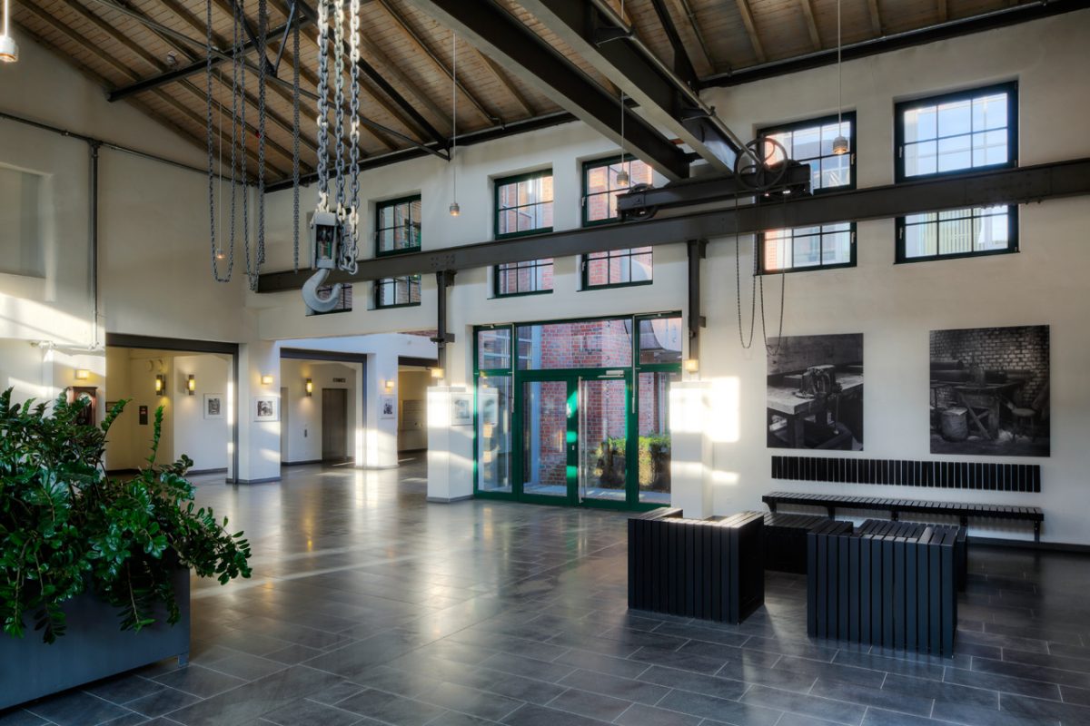Foyer mit Kranhaken, Stahlträgern und Sitzbänken im Eingangsbereich.