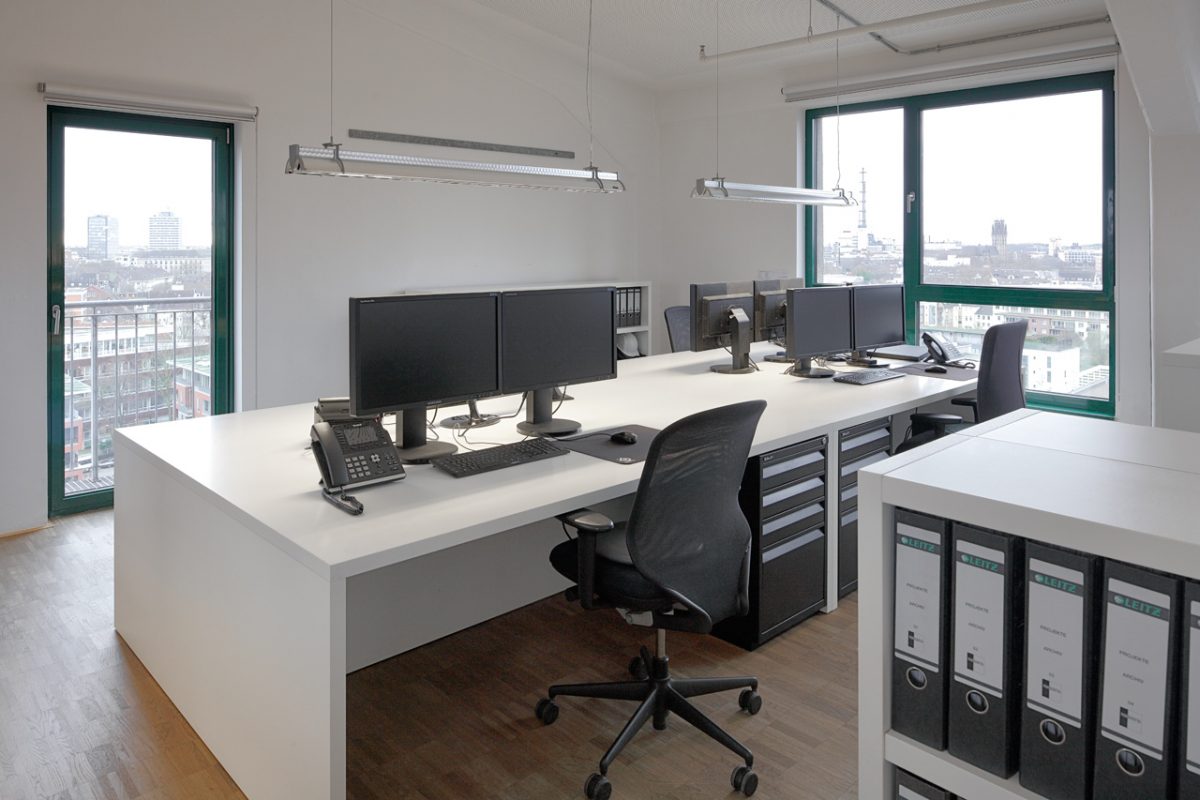 Modernes Großraumbüro mit Schreibtischen, Monitoren und Aktenregalen.