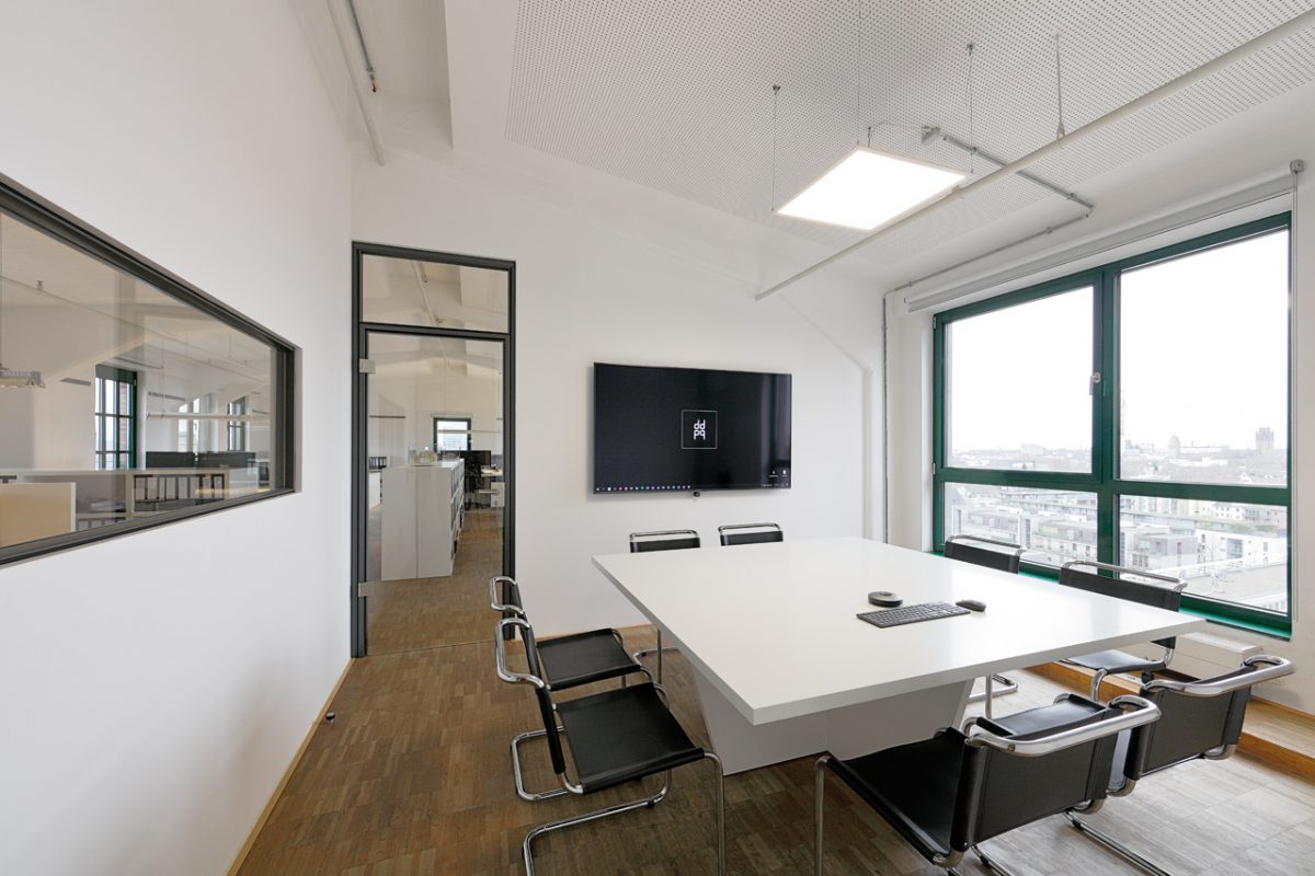 Heller Konferenzraum mit großem Bildschirm und Ausblick über die Stadt.