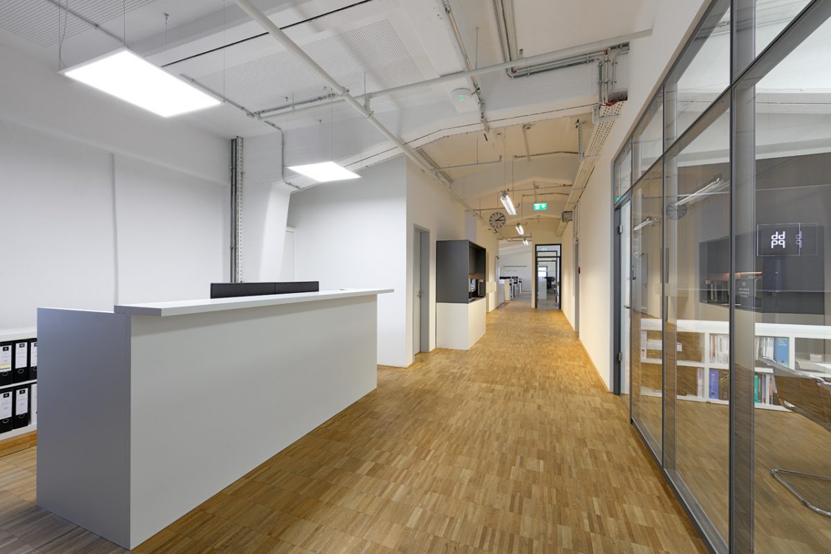 Moderner Büroflur mit Empfangstresen, Glastrennwänden und Parkettboden.