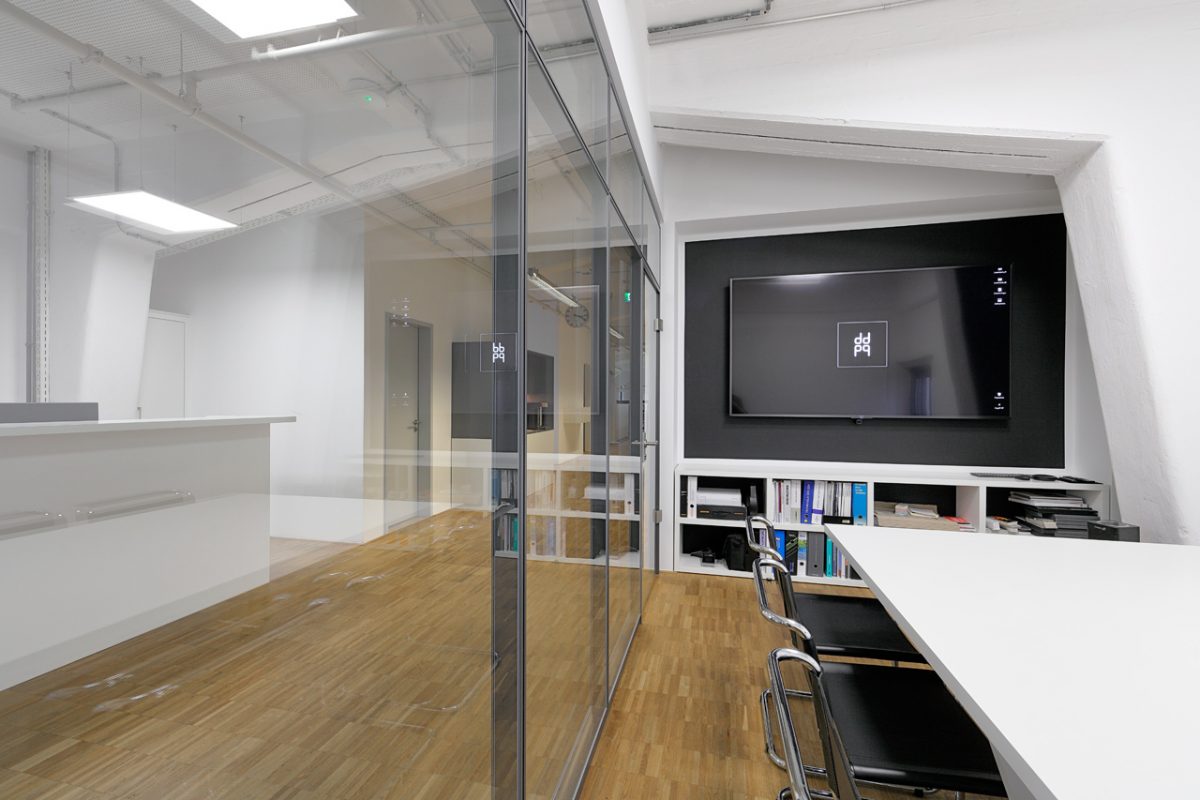 Besprechungsraum mit Glastrennwand, Bildschirm und Bücherregal.