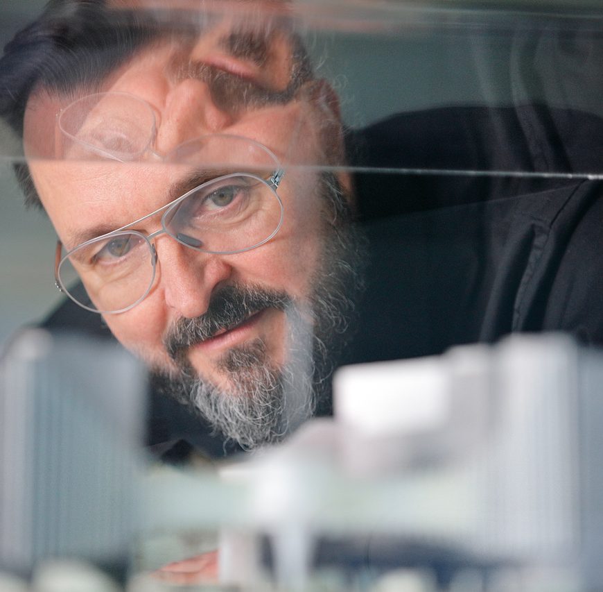 Mann mit Brille blickt durch Glas auf ein Architekturmodell