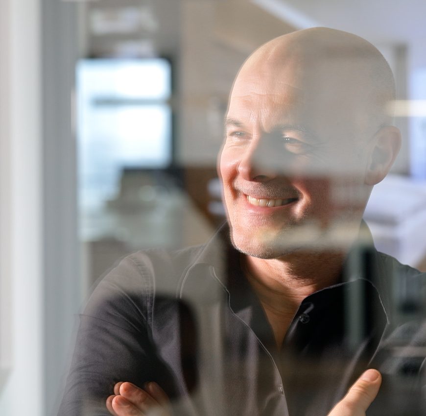 Lächelnder Mann mit verschränkten Armen hinter reflektierender Glasscheibe