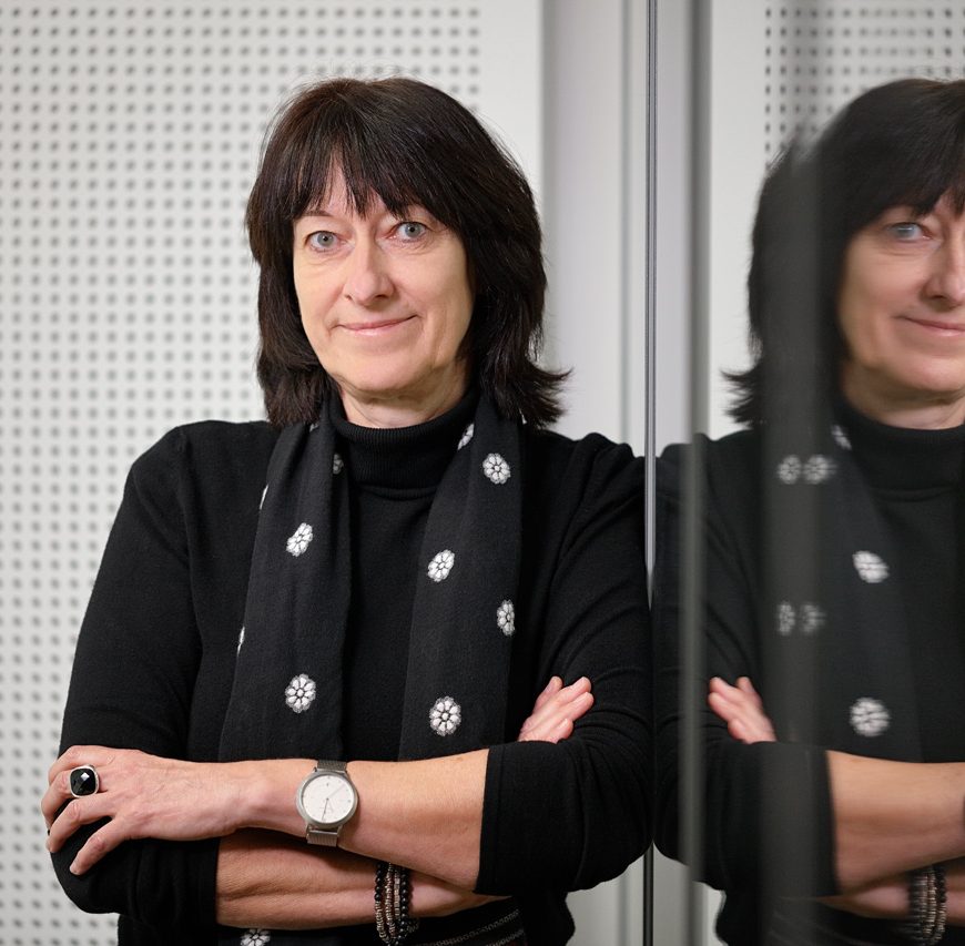 Frau mit verschränkten Armen steht vor Glaswand mit Spiegelung