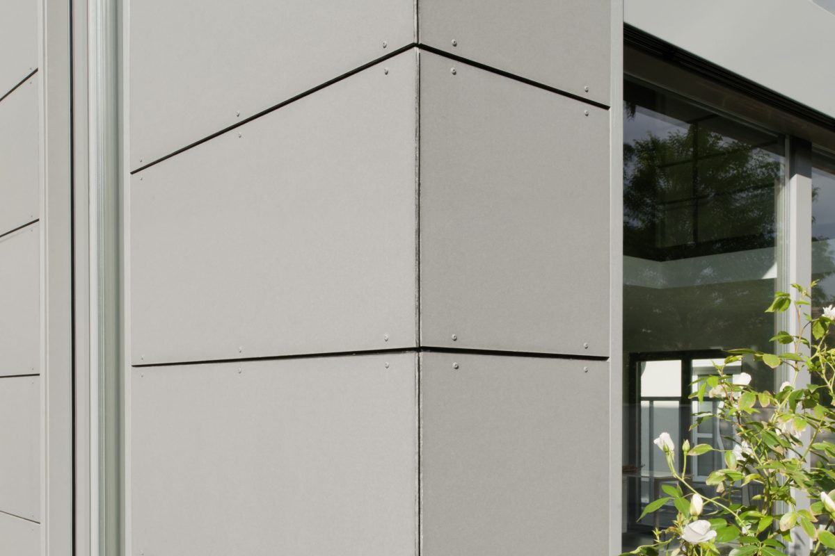 Moderne Hausecke mit grauer Vorhangfassade und großen Fenstern.