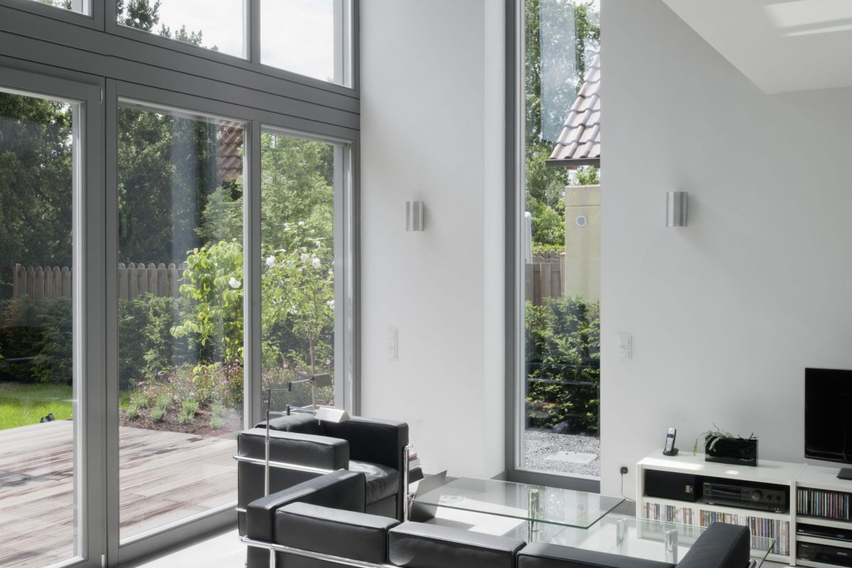 Wohnzimmer mit Glasfront, schwarzem Sofa und Blick auf den Garten.