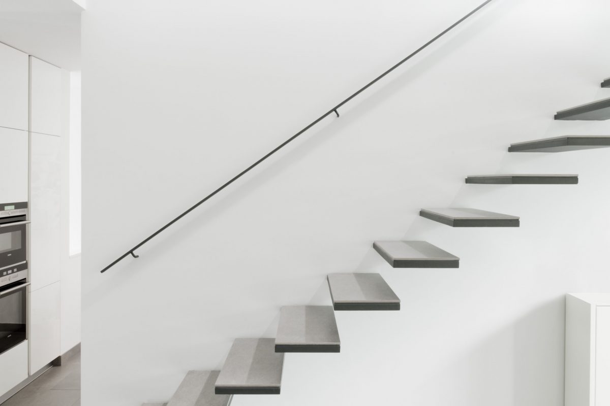 Minimalistische Treppe mit Wandhandlauf vor weißer Wand