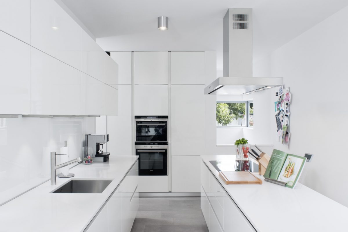 Moderne weiße Küche mit Kochinsel, Einbaugeräten und Dunstabzugshaube
