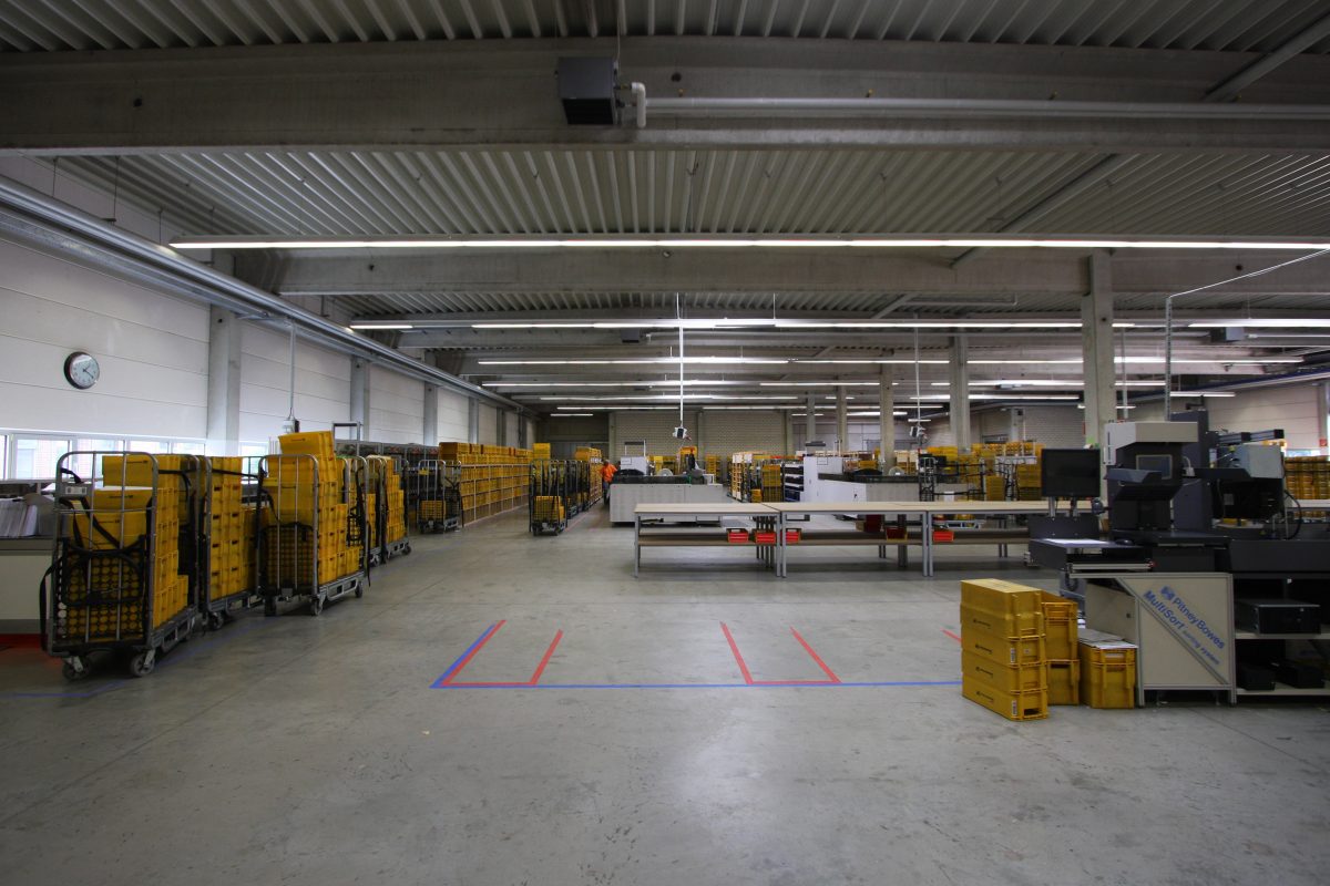 Sortierzentrum mit gelben Postkisten, Tischen und markiertem Bodenbereich