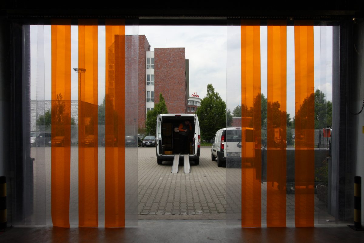 Blick durch orange Lamellenvorhänge auf geparkte Lieferwagen am Hintereingang