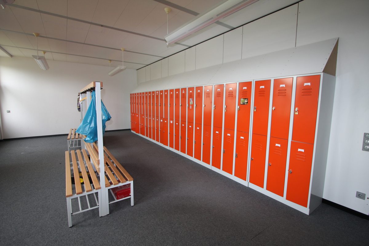 Umkleideraum mit orangefarbenen Spinden und Holzbänken mit Garderobenleiste