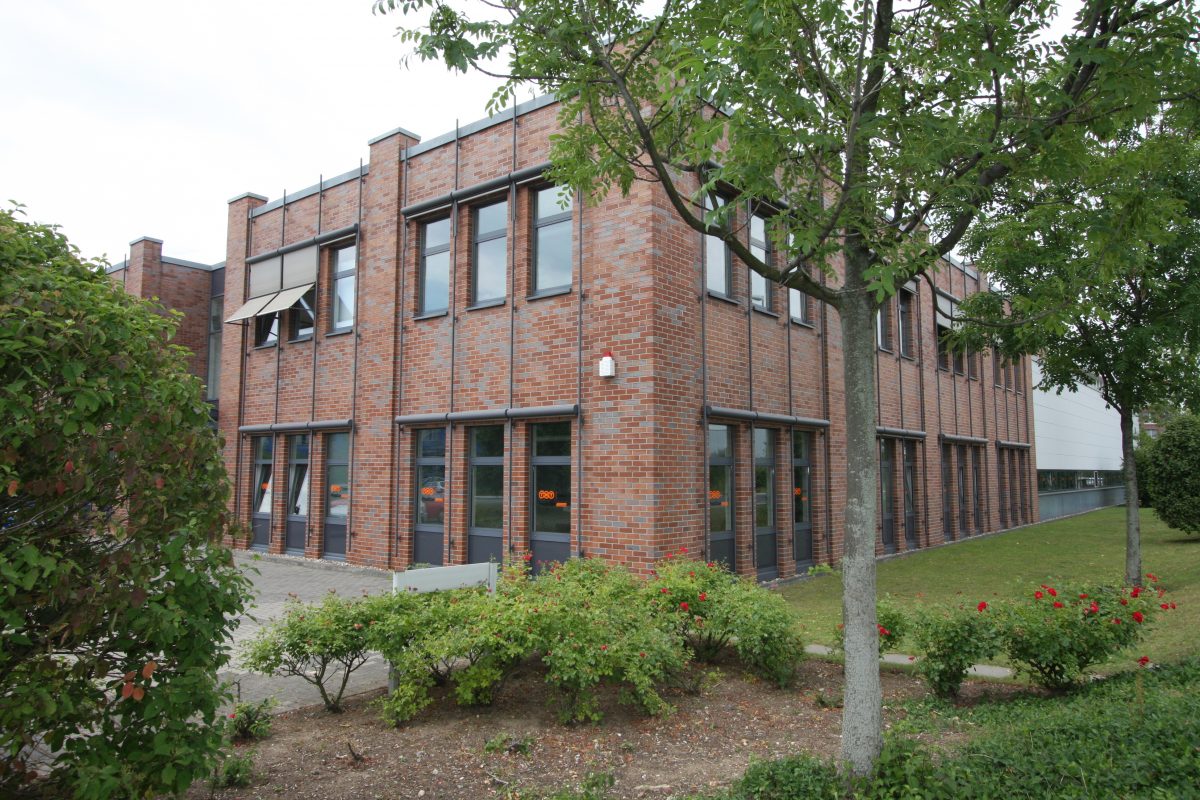 Übereckansicht Ziegelfassade mit großen Fenstern und begrünter Außenanlage