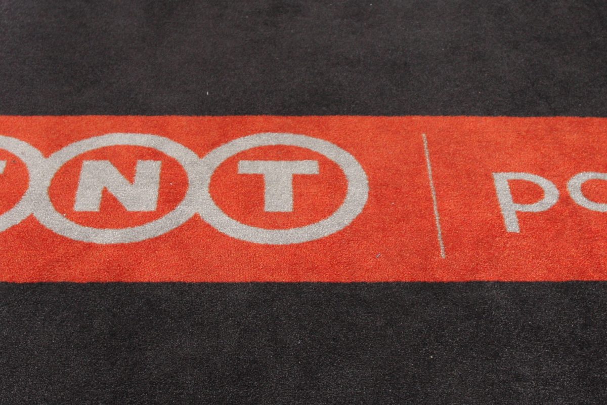 Schwarze Fußmatte mit rotem TNT Post-Logo auf dem Eingangsbereich