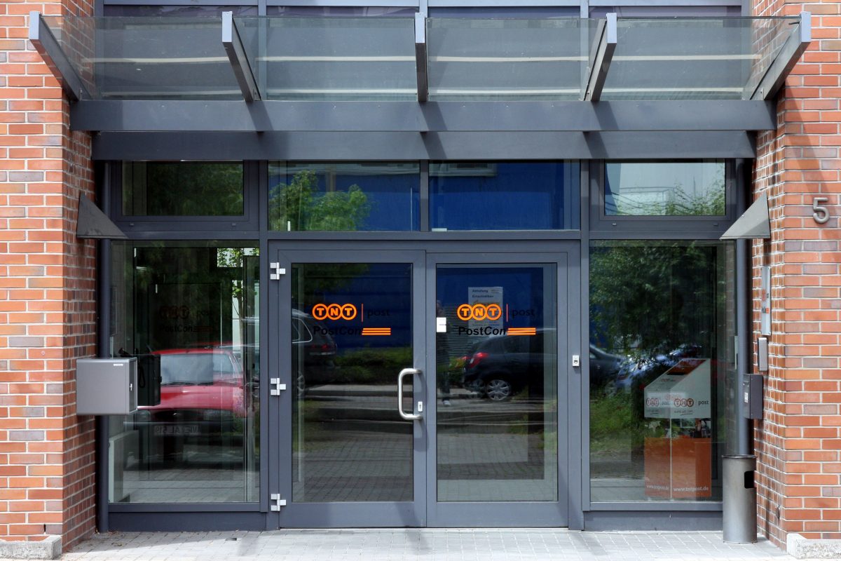 Glaseingang von TNT Post mit Logo und moderner Überdachung