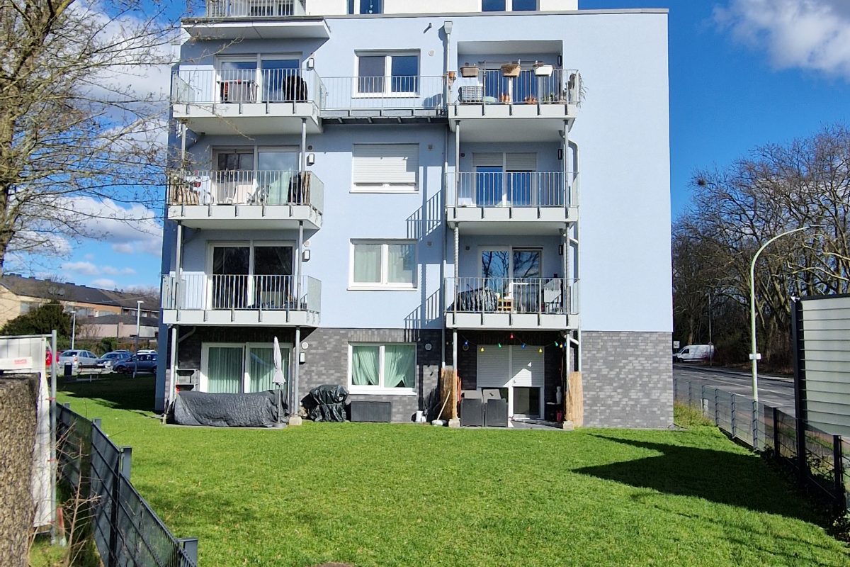 Modernes Wohnhaus mit Balkonen und gepflegter Rasenfläche davor.