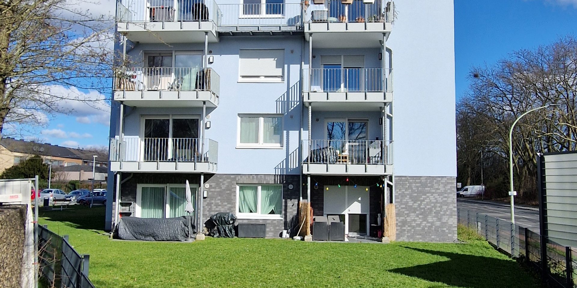 Modernes Wohnhaus mit Balkonen und gepflegter Rasenfläche davor.