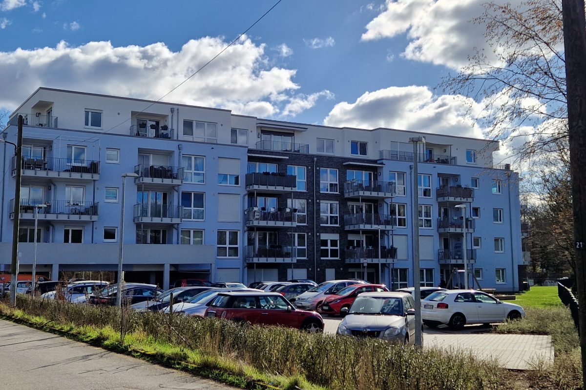 Modernes Mehrfamilienhaus mit Balkonen und vorgelagertem Parkplatz.